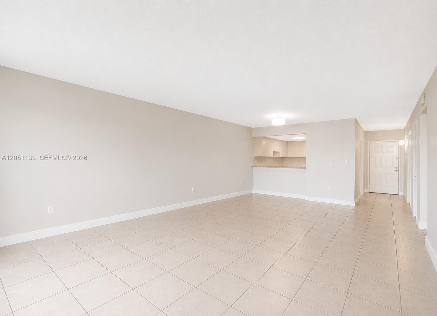 An empty living area features beige tile floors, light-colored walls, and an open kitchen pass-through — 6940 Miami Gardens Dr # 531, Hialeah FL 33015, HIALEAH, FL