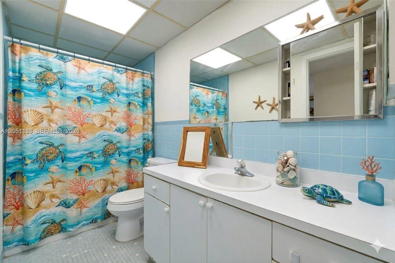 A bathroom features a sea-themed shower curtain, blue tiled walls, and a white vanity — 6940 Miami Gardens Dr # 531, Hialeah FL 33015, HIALEAH, FL