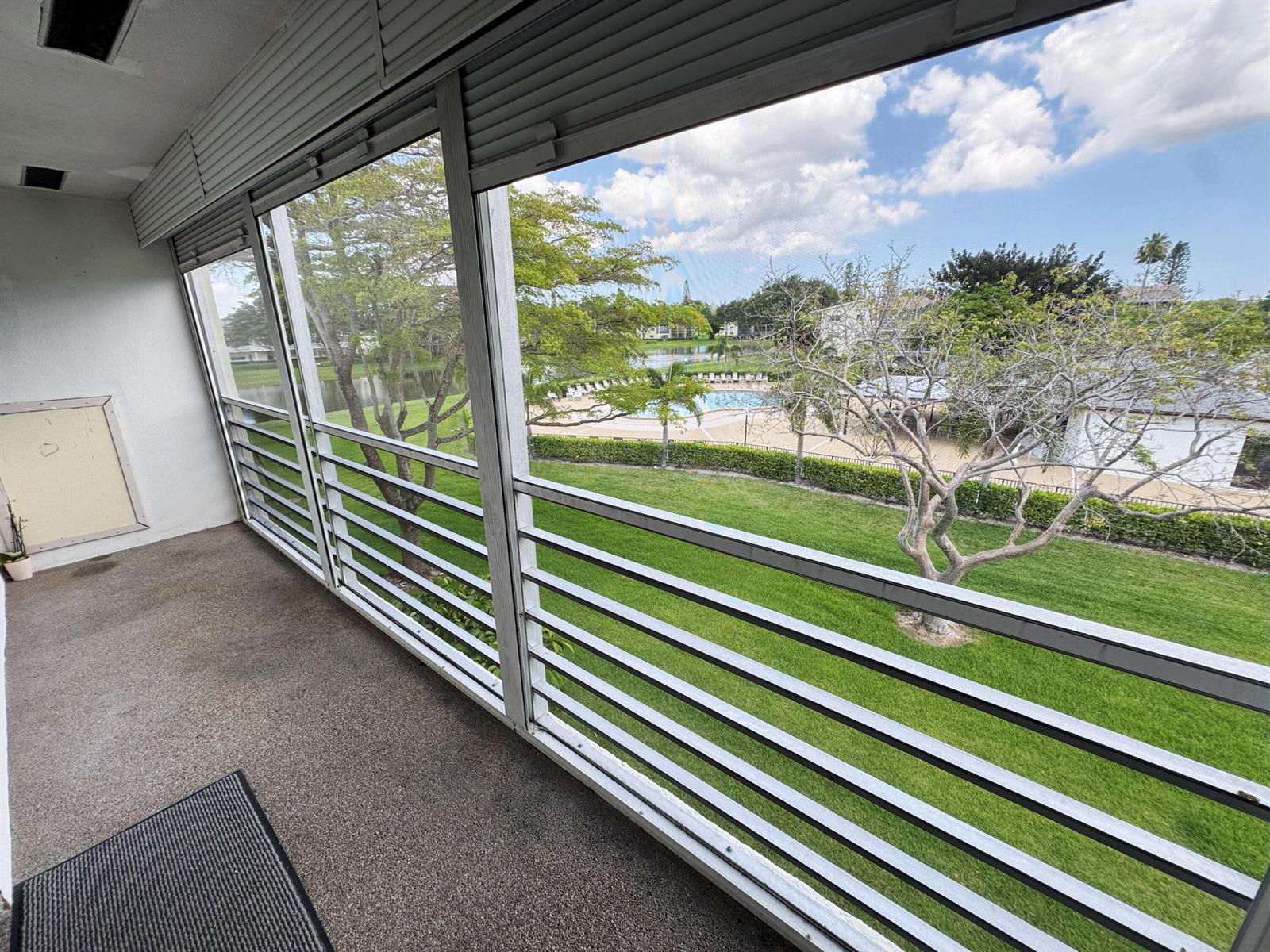 A screened-in balcony overlooks a grassy lawn, a swimming pool, and a small lake — 125 Dorset C, Boca Raton FL 33434, BOCA RATON, FL