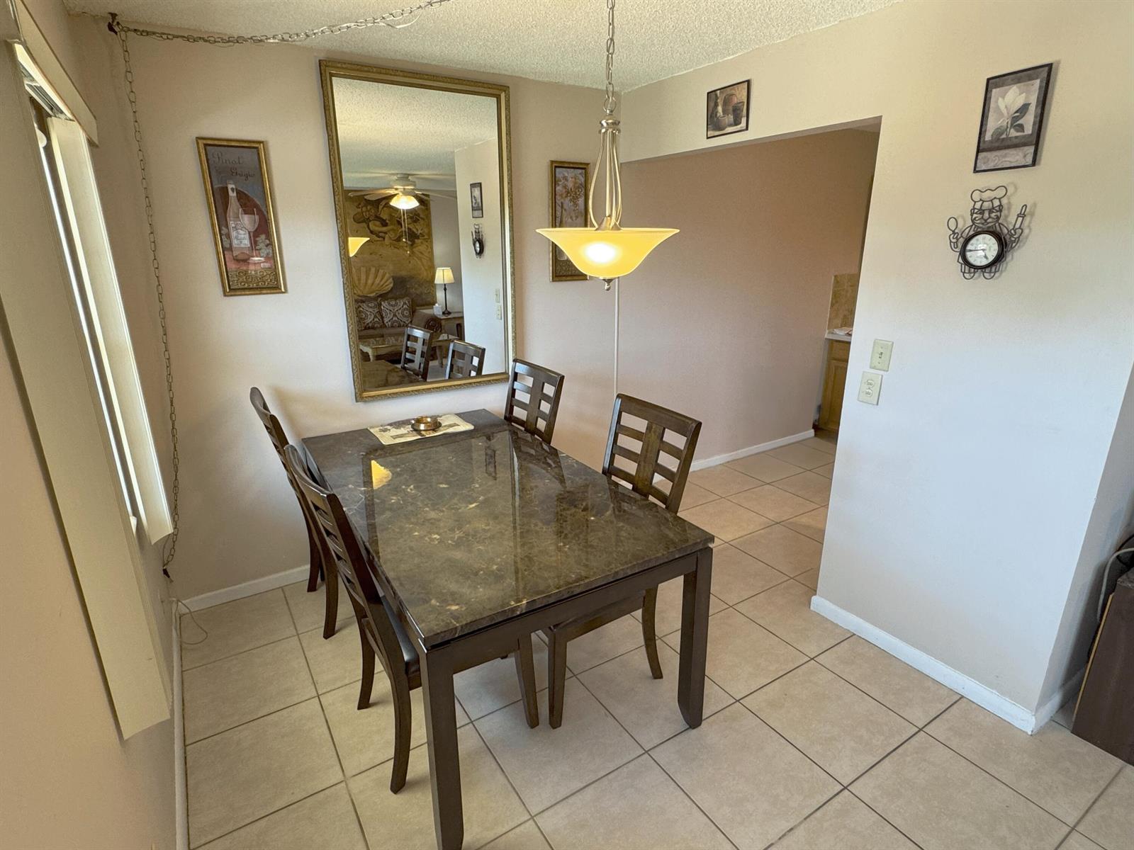 A dining room features a dark marble-topped table, four chairs, a mirror, and tile flooring — 125 Dorset C, Boca Raton FL 33434, BOCA RATON, FL