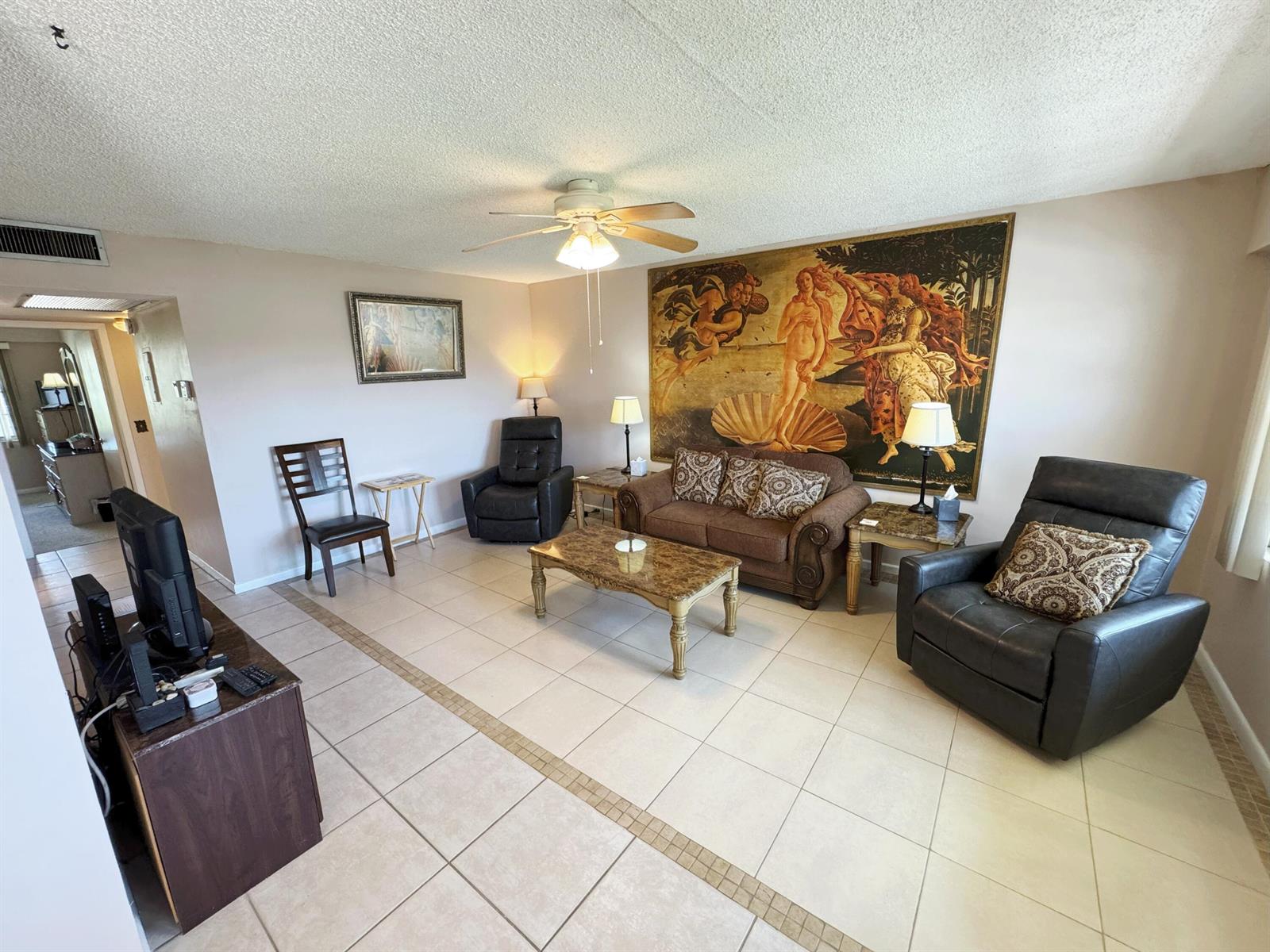 A living room features tile flooring, a ceiling fan, leather recliners, and a large wall tapestry — 125 Dorset C, Boca Raton FL 33434, BOCA RATON, FL