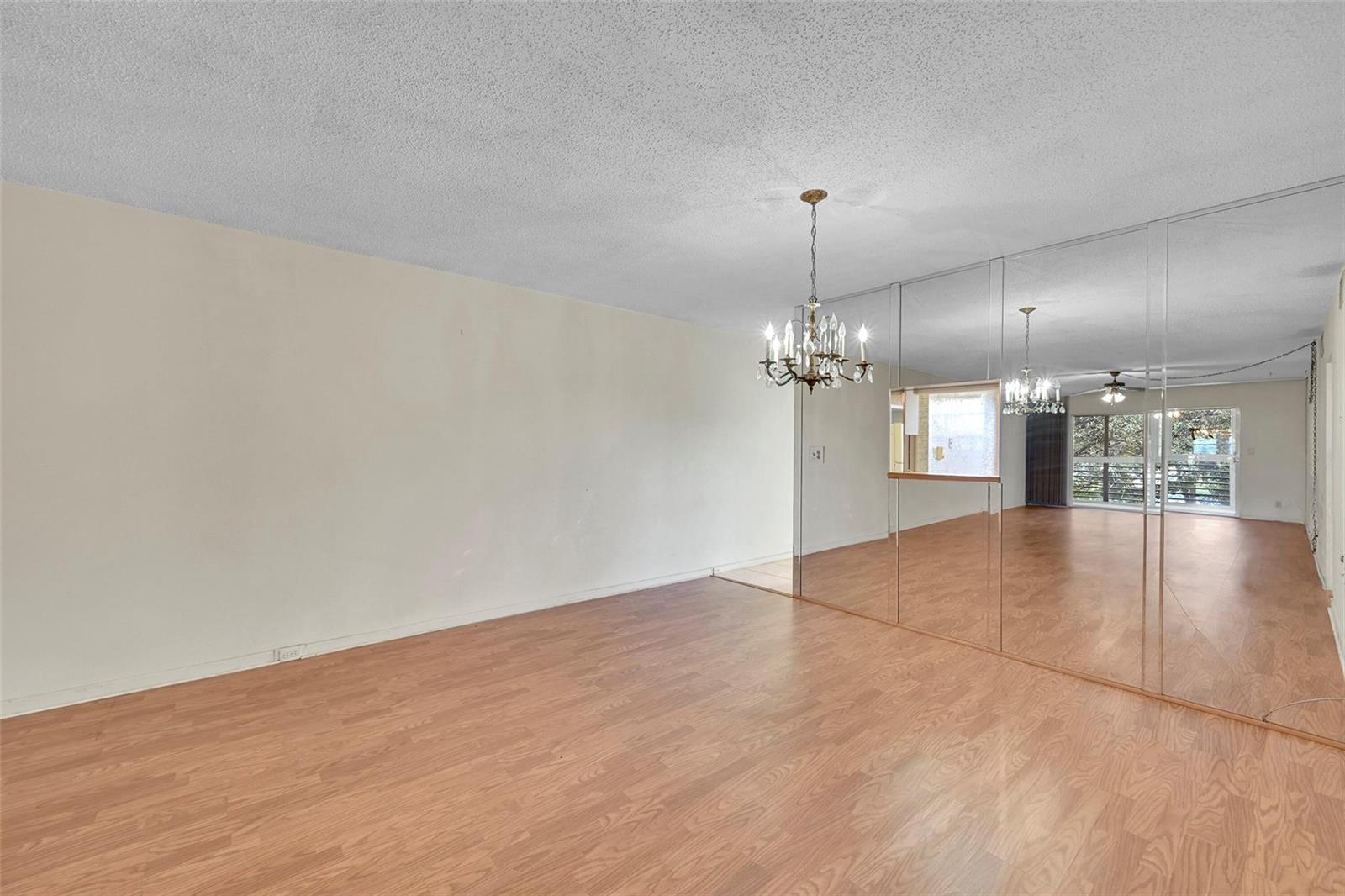 An empty room with wood-look flooring, a chandelier, and a large mirrored wall — 2006 Granada Drive # A3, Coconut Creek FL 33066, COCONUT CREEK, FL