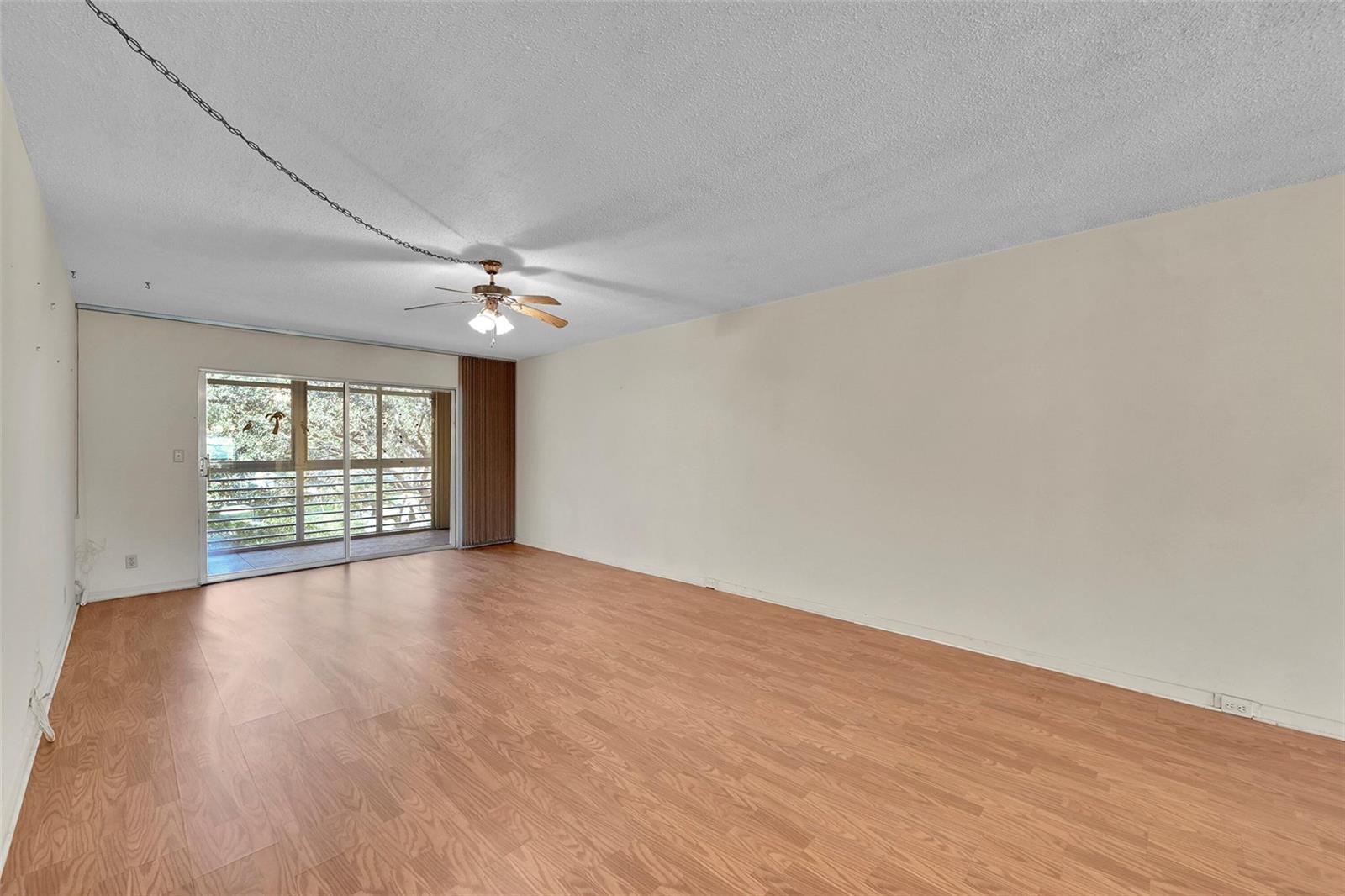 An empty living room features light wood-look flooring, a ceiling fan, and a sliding glass door — 2006 Granada Drive # A3, Coconut Creek FL 33066, COCONUT CREEK, FL
