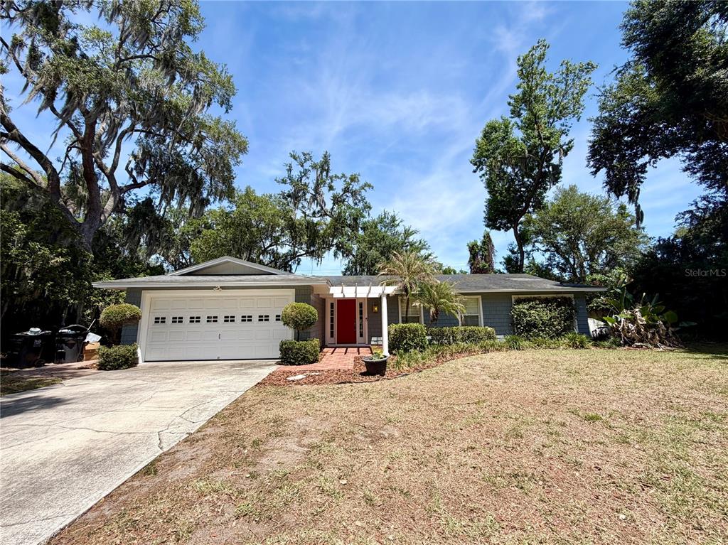 A single-story house with a white garage, red front door, and mature trees — 6322 OAK SQUARE E, LAKELAND, FL