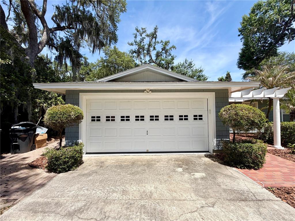 A detached garage with a white door, shingled siding, and manicured shrubs on a driveway — 6322 OAK SQUARE E, LAKELAND, FL