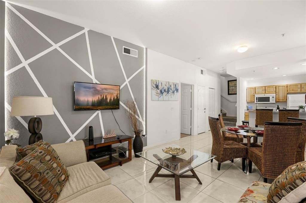 A living room features a geometric accent wall, a glass coffee table, and an adjacent kitchen — 4005 VENETIAN BAY DRIVE UNIT 108, KISSIMMEE, FL