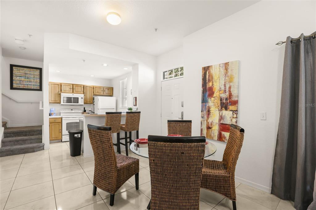 A dining area with a glass table and wicker chairs sits adjacent to a kitchen — 4005 VENETIAN BAY DRIVE UNIT 108, KISSIMMEE, FL