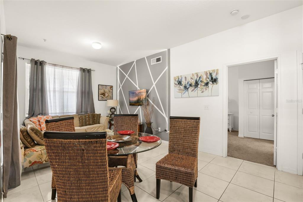A dining area with wicker chairs and a glass table sits before a living room — 4005 VENETIAN BAY DRIVE UNIT 108, KISSIMMEE, FL