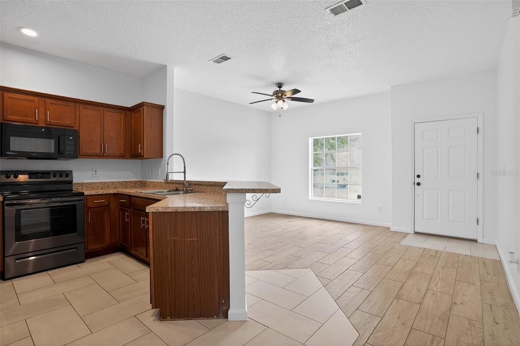 A kitchen with wood cabinets and a breakfast bar opens into a living area — 1923 YELLOWFIN DRIVE, PORT ORANGE, FL