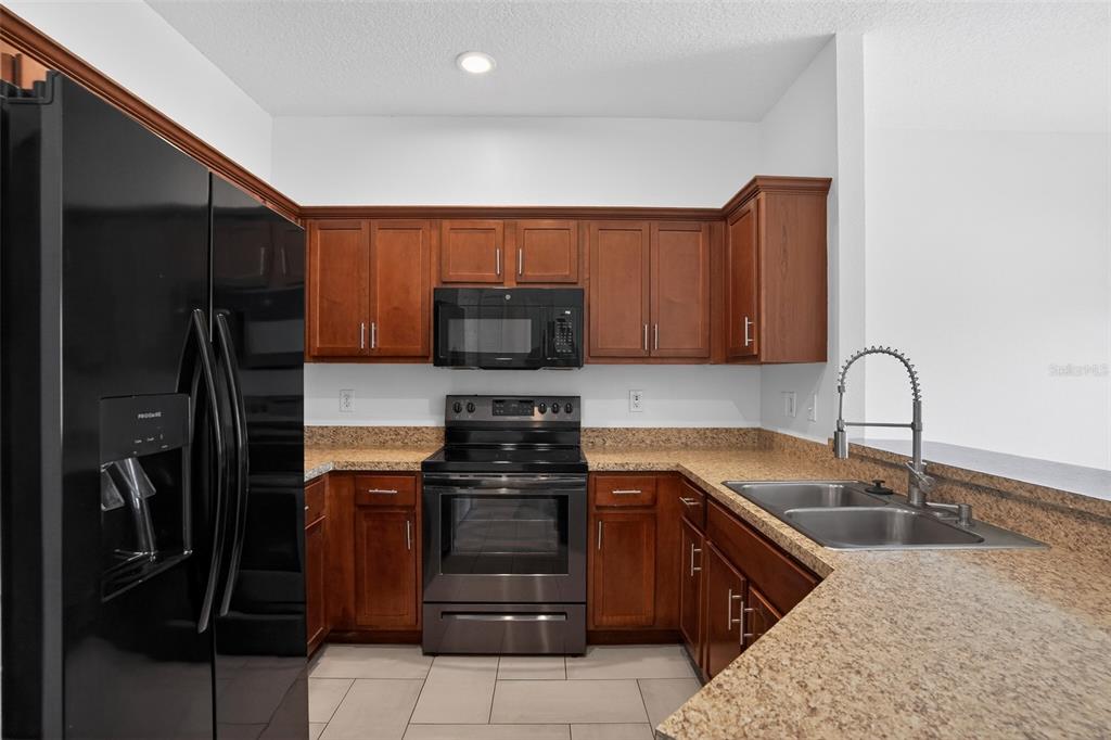 A kitchen features wood cabinets, granite countertops, stainless steel appliances, and a black refrigerator — 1923 YELLOWFIN DRIVE, PORT ORANGE, FL