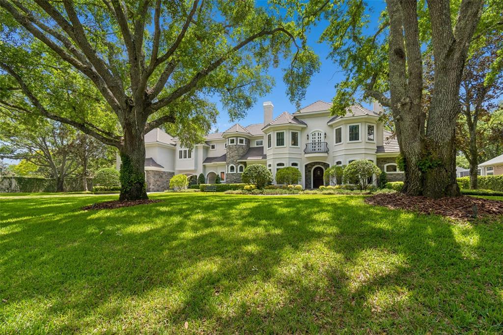 A large, multi-story house with a stone and stucco exterior sits behind a grassy lawn — 702 BERROCALES DE AVILA, TAMPA, FL