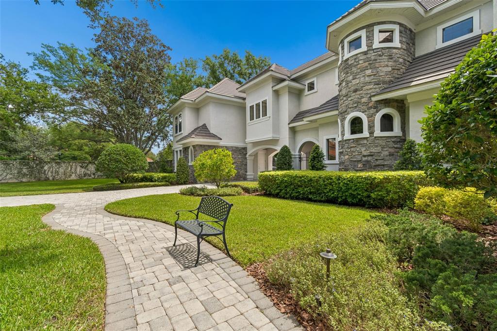 A stone and stucco house features a curved tower, arched windows, and a paved walkway — 702 BERROCALES DE AVILA, TAMPA, FL