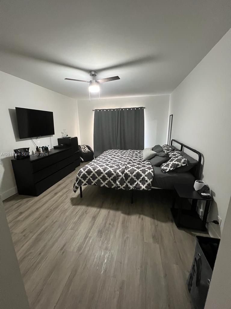 This bedroom features light wood-look flooring, a ceiling fan, and a black metal bed frame — 18051 NW 68th Ave # K103, Hialeah FL 33015, HIALEAH, FL