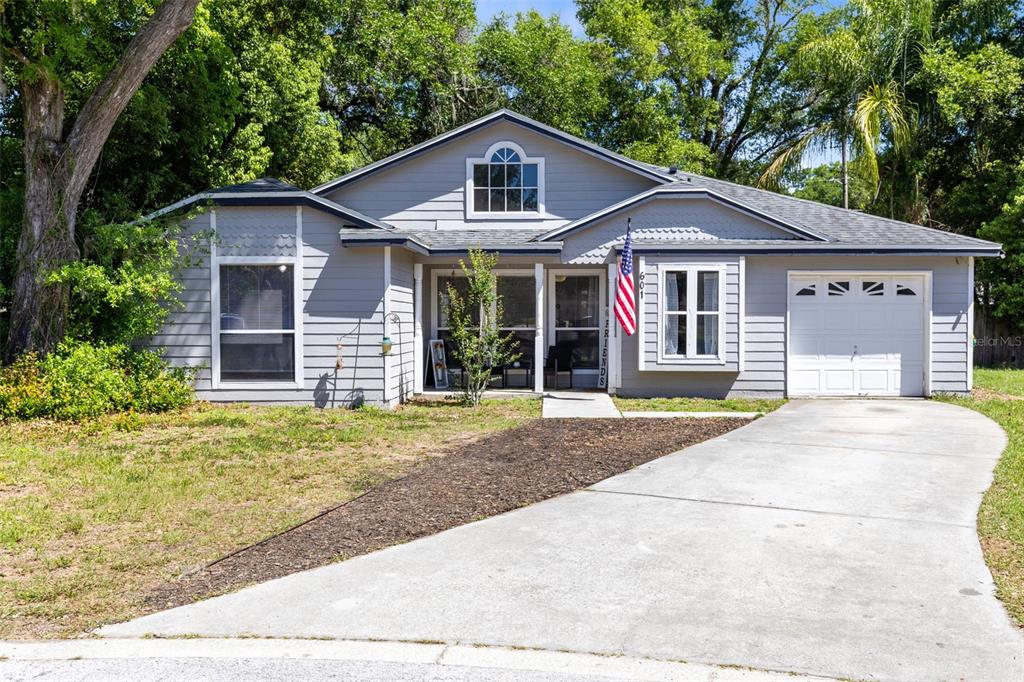 A single-story gray house with a concrete driveway, a front porch, and an American flag — 601 ARLINGTON COURT, EUSTIS, FL