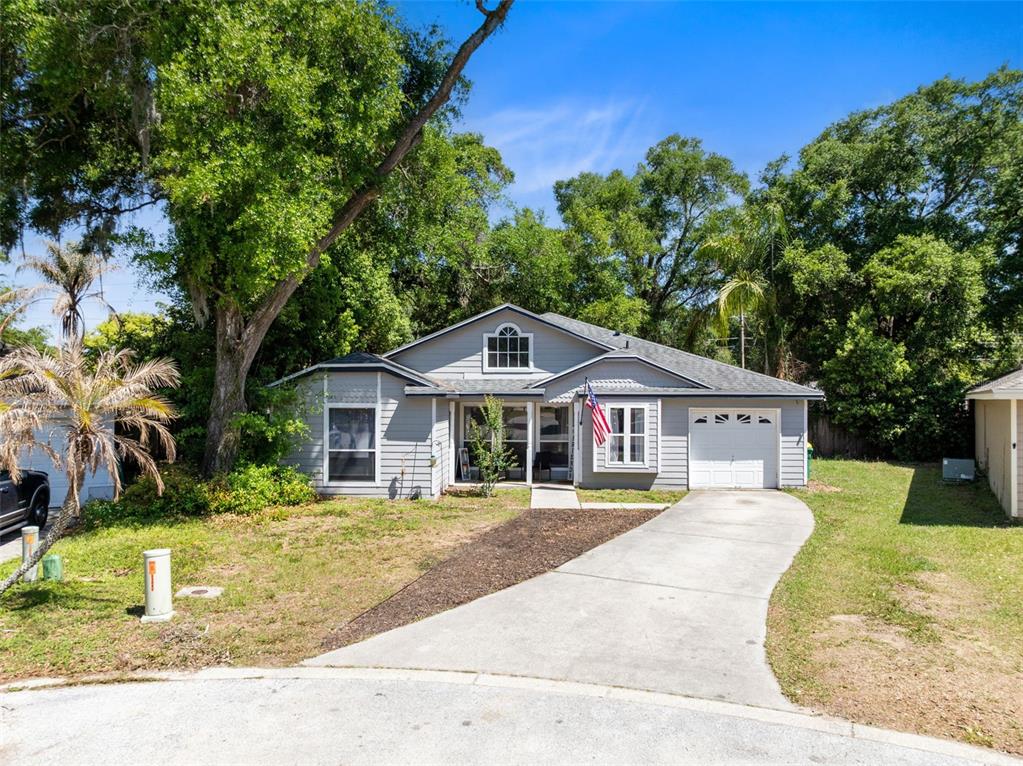 A single-story gray house with a concrete driveway, a front garage, and mature trees — 601 ARLINGTON COURT, EUSTIS, FL