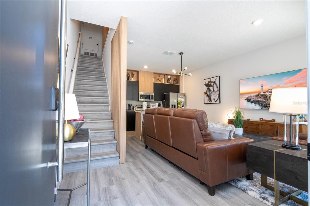 A living room with a brown leather sofa, wood-look flooring, and stairs with wood slats — 3389 TRANQUIL TRAIL, KISSIMMEE, FL