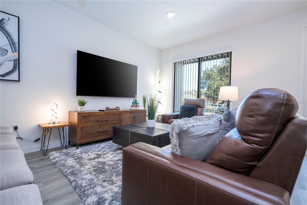 A living room features a wall-mounted television, a wooden media console, and leather seating — 3389 TRANQUIL TRAIL, KISSIMMEE, FL