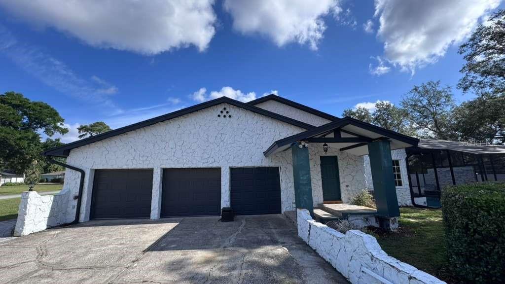 A white stucco house features a three-car garage and a covered front entryway — 4627 WOODLOT COURT, ORLANDO, FL