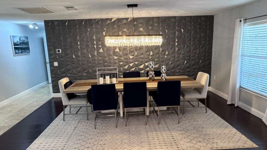 A dining room features a dark geometric accent wall, a long table, and a crystal chandelier — 4627 WOODLOT COURT, ORLANDO, FL