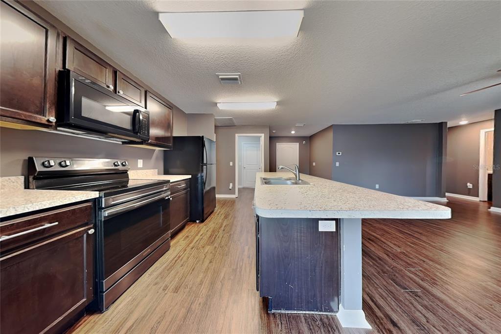A kitchen features dark wood cabinets, black appliances, and a large island with granite countertops — 26463 MOTT AVENUE, BROOKSVILLE, FL