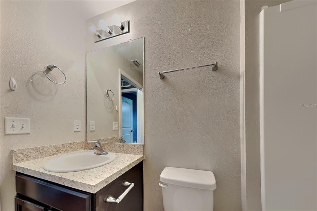 A bathroom features a dark vanity with a speckled countertop, a mirror, and a toilet — 26463 MOTT AVENUE, BROOKSVILLE, FL