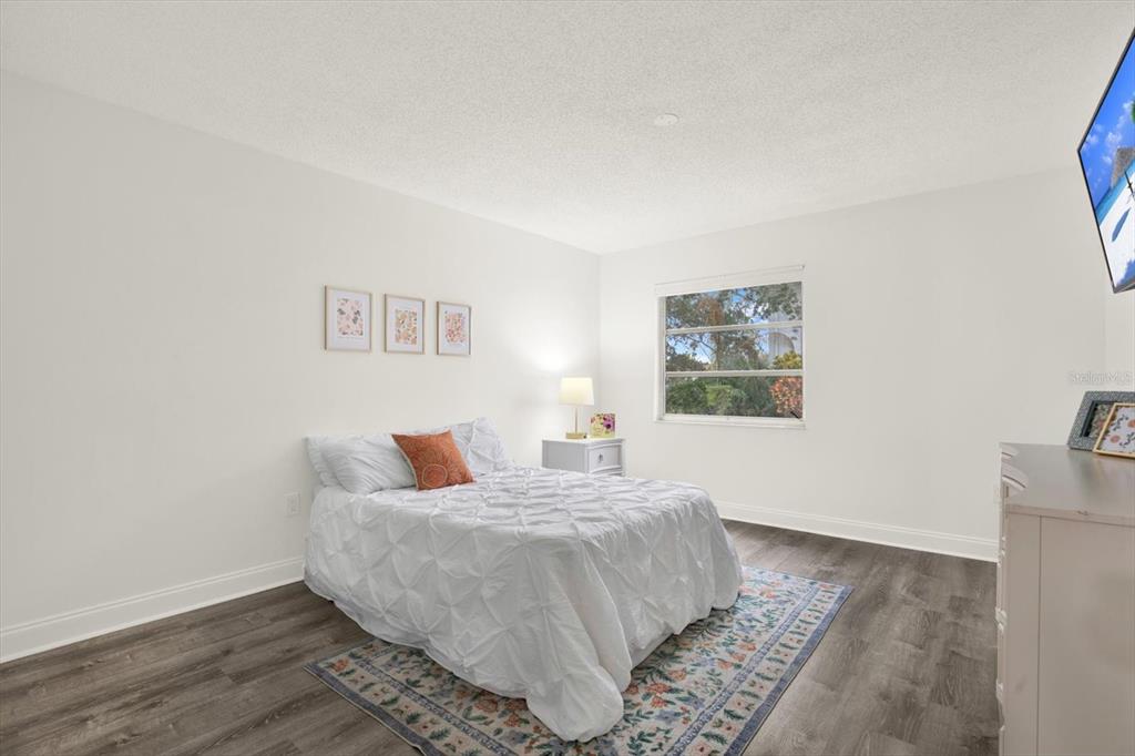 A bedroom features a white bed, a patterned rug, and a window on a white wall — 235 S MCMULLEN BOOTH ROAD UNIT 45, CLEARWATER, FL