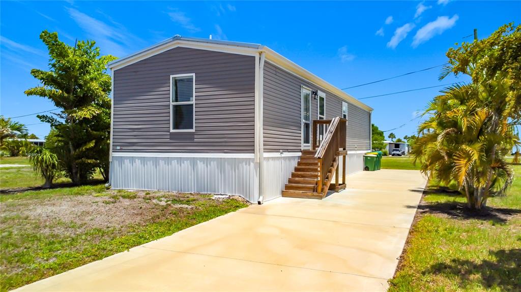A gray manufactured home with a concrete driveway and wooden stairs leading to the entrance — 1433 SEAGULL DRIVE, ENGLEWOOD, FL