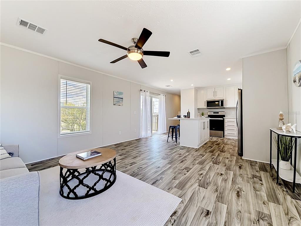 An open-concept living room and kitchen featuring wood-look flooring, a ceiling fan, and white cabinetry — 1433 SEAGULL DRIVE, ENGLEWOOD, FL