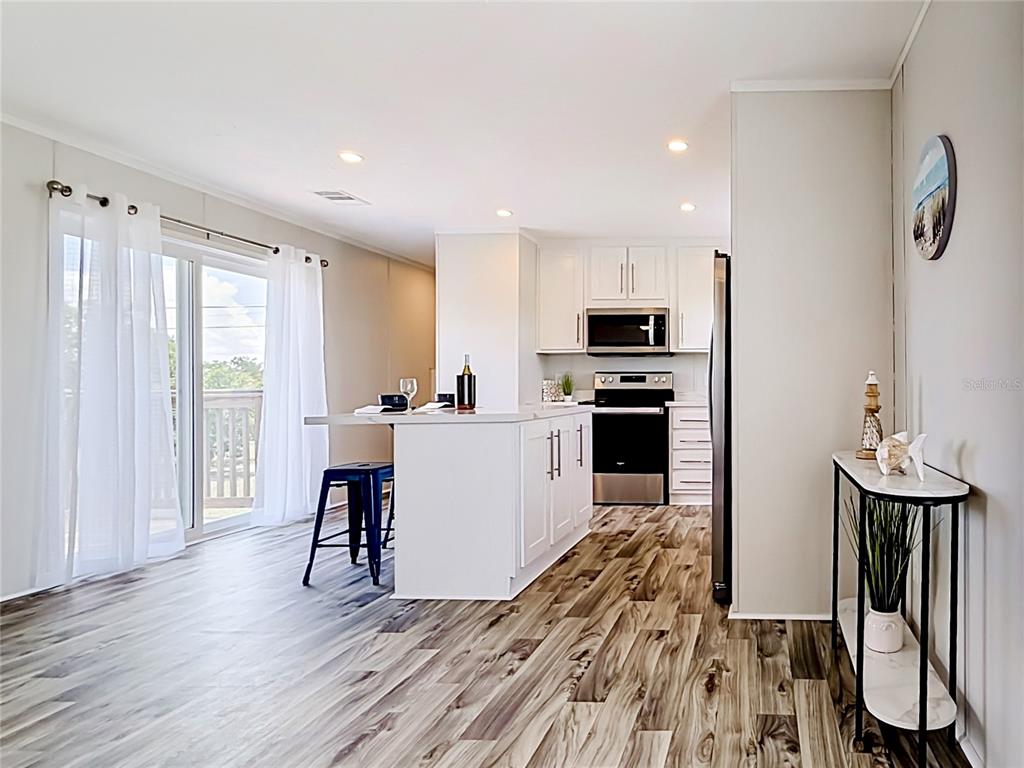 A kitchen with white cabinets, a central island, and wood-look flooring opens to a patio — 1433 SEAGULL DRIVE, ENGLEWOOD, FL