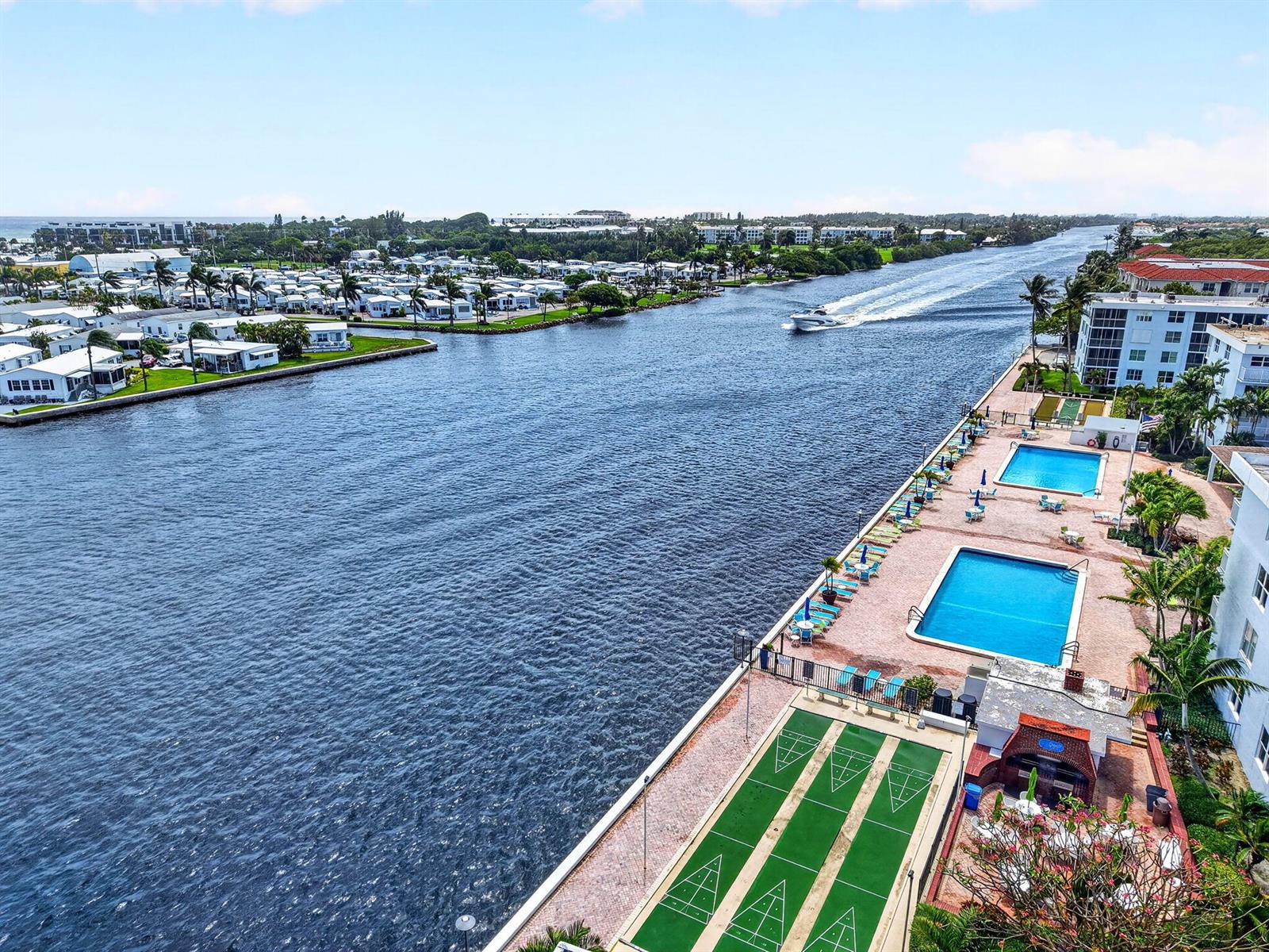 An aerial view shows a waterway with a boat, two swimming pools, and shuffleboard courts — 2016 S Federal Highway # E309, Boynton Beach FL 33435, BOYNTON BEACH, FL