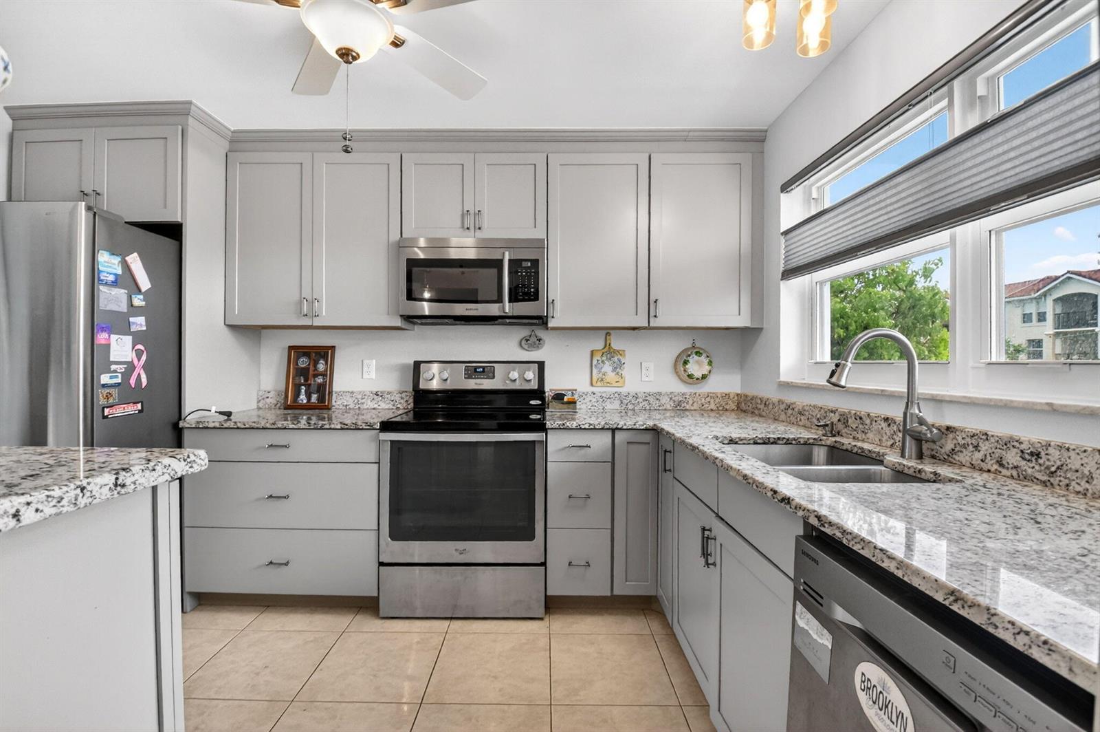A kitchen features gray cabinets, granite countertops, stainless steel appliances, and tile flooring — 2016 S Federal Highway # E309, Boynton Beach FL 33435, BOYNTON BEACH, FL