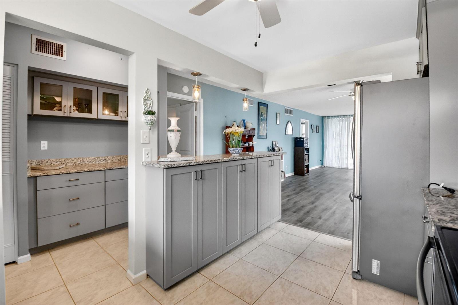 A kitchen with grey cabinets and granite countertops opens into a living area with flooring — 2016 S Federal Highway # E309, Boynton Beach FL 33435, BOYNTON BEACH, FL