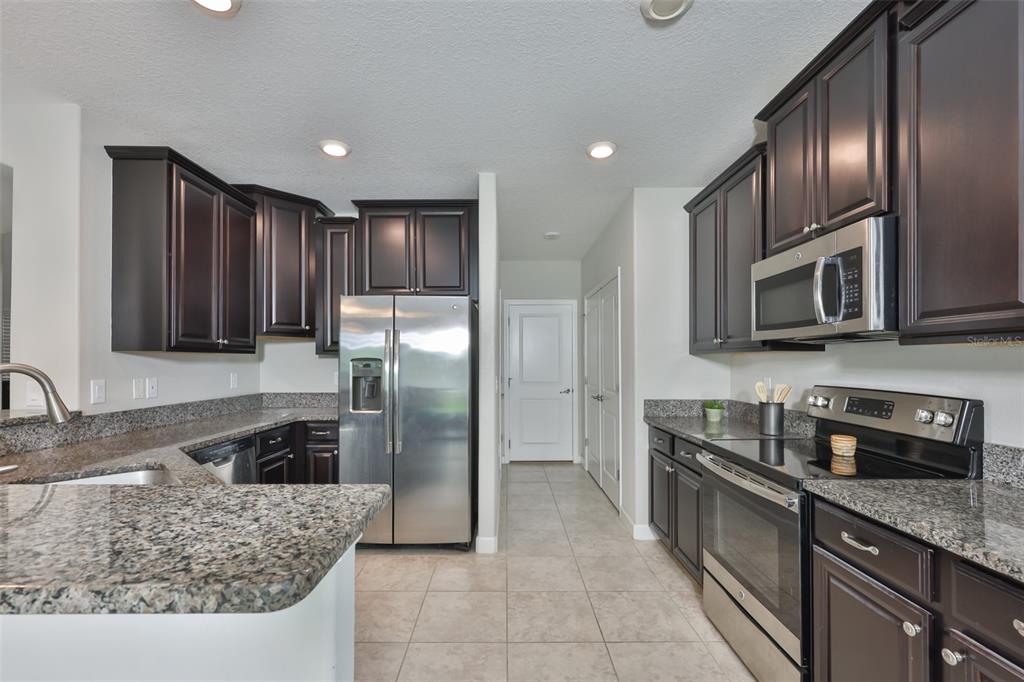 A kitchen features dark wood cabinets, granite countertops, stainless steel appliances, and tile flooring — 1922 CITRUS LAKE COURT, RUSKIN, FL
