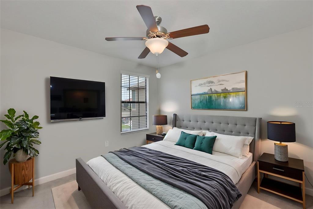 A bedroom features a gray upholstered bed, a ceiling fan, a wall-mounted television, and artwork — 1922 CITRUS LAKE COURT, RUSKIN, FL