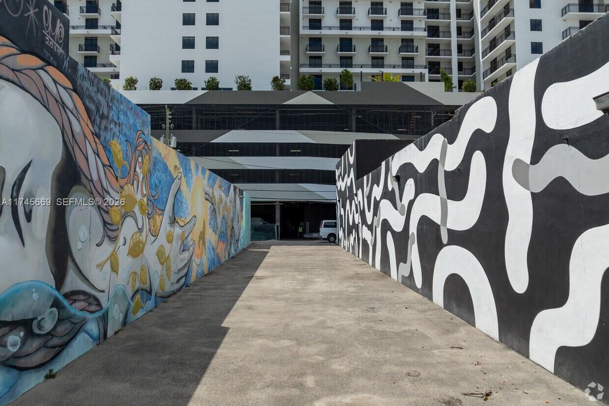 A narrow concrete alleyway is flanked by two walls featuring large-scale black and white murals — 2020 Harrison St, Hollywood FL 33020, HOLLYWOOD, FL