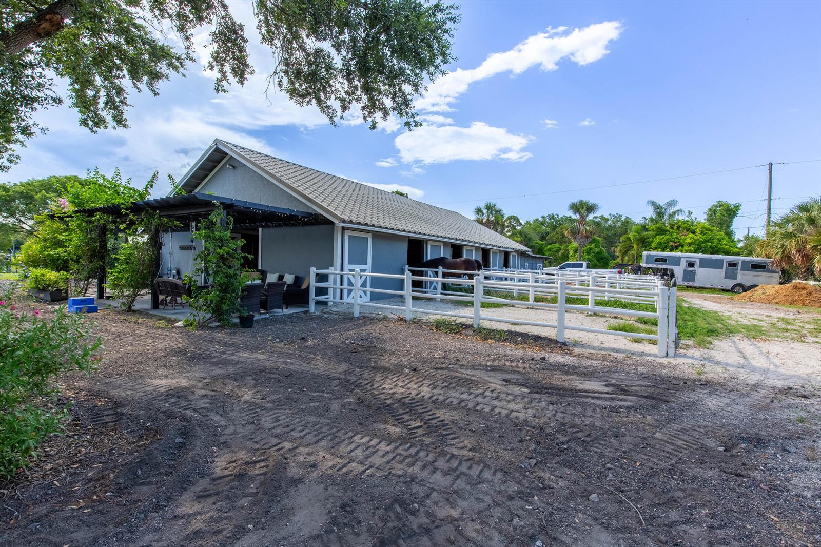 A gray horse barn with a covered patio and white fencing sits on a dirt lot — 844 Arabian Drive, Loxahatchee FL 33470, LOXAHATCHEE, FL