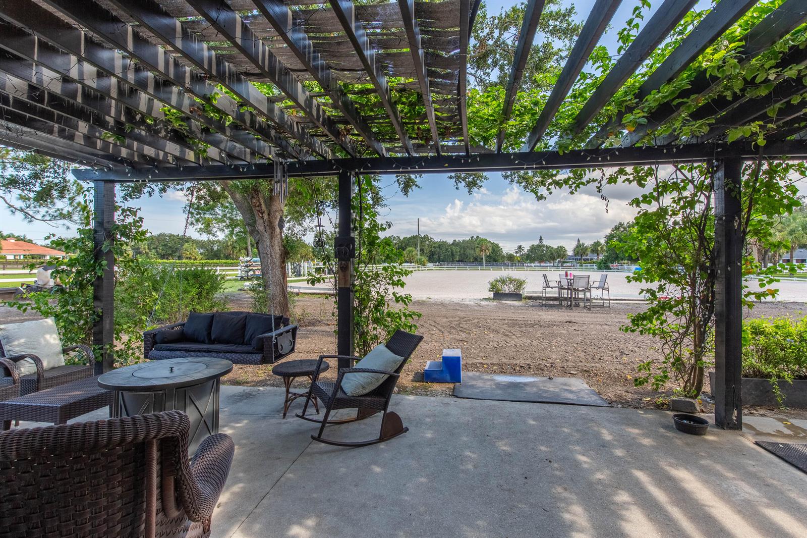 A covered patio features wicker furniture, a fire pit, and a view of an equestrian arena — 844 Arabian Drive, Loxahatchee FL 33470, LOXAHATCHEE, FL