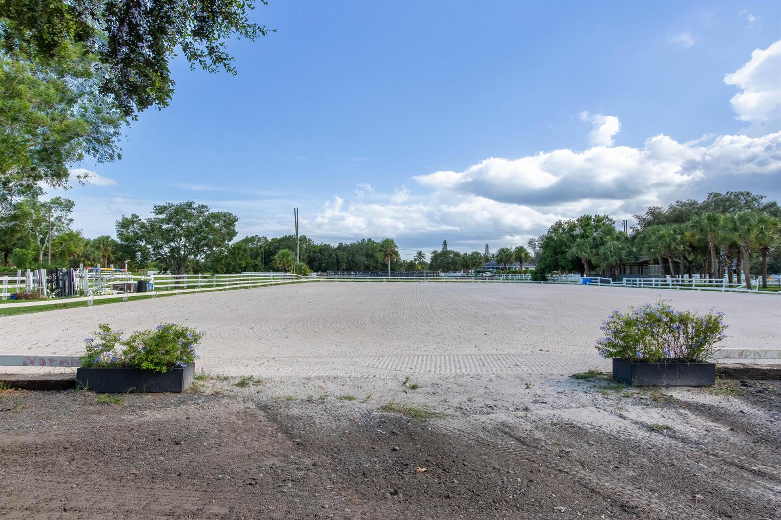 A large, raked sand equestrian riding arena is enclosed by white fencing under a blue sky — 844 Arabian Drive, Loxahatchee FL 33470, LOXAHATCHEE, FL
