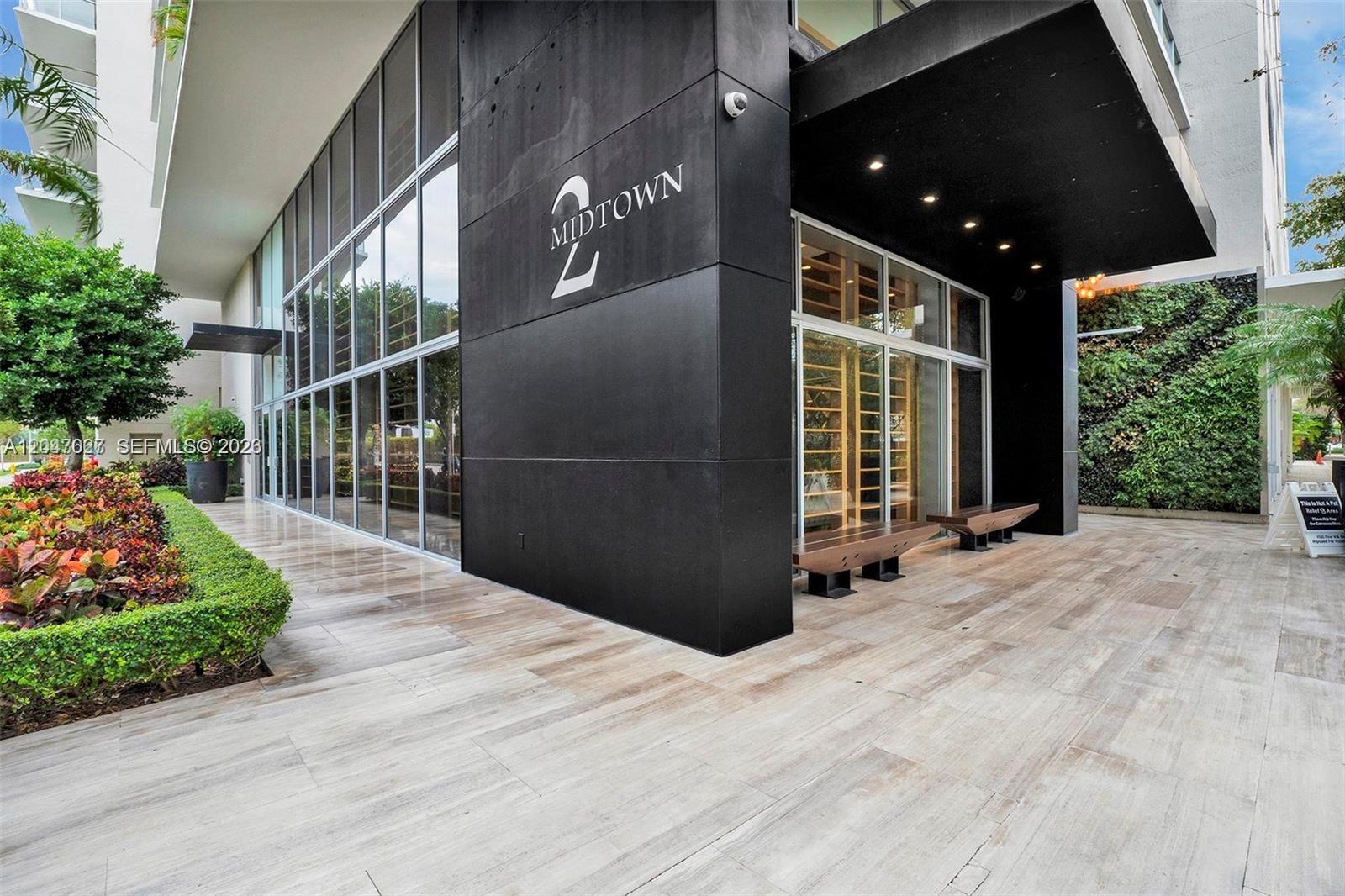 The exterior entrance of a modern building features a black wall with signage and landscaping — 3470 E Coast Ave # H0904, Miami FL 33137, MIAMI, FL