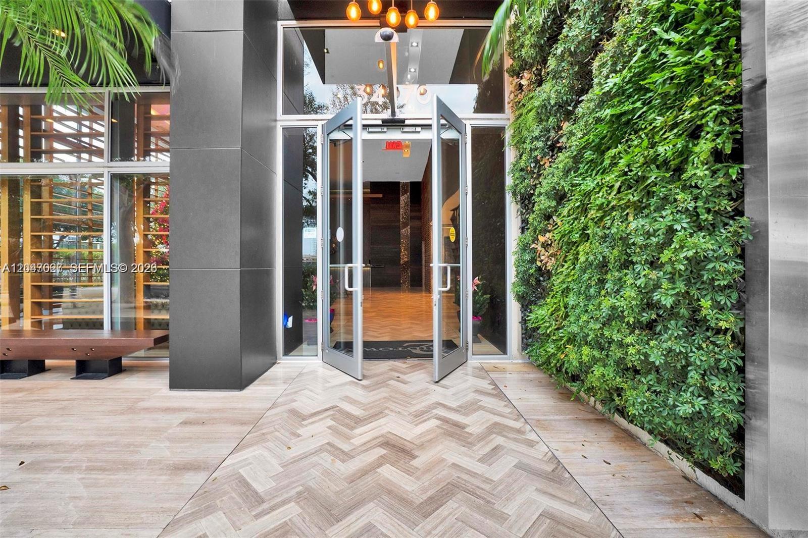 The entrance features a herringbone-patterned floor, glass double doors, and a vertical garden wall — 3470 E Coast Ave # H0904, Miami FL 33137, MIAMI, FL
