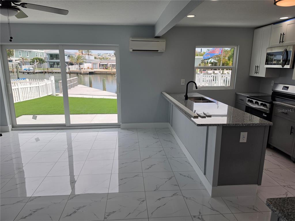 A kitchen with white cabinets, granite countertops, and tile flooring overlooks a canal and yard — 145 131 AVENUE E UNIT 2, MADEIRA BEACH, FL