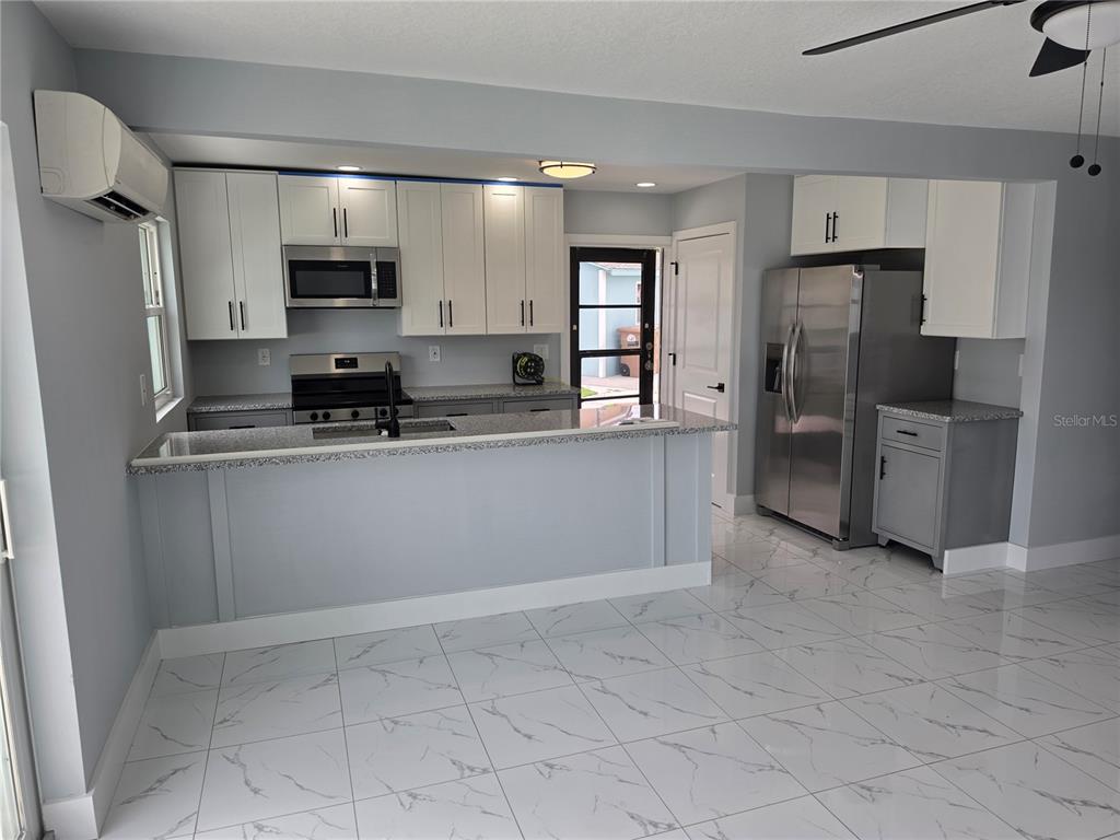 A kitchen features white upper cabinets, grey lower cabinets, stainless steel appliances, and tiled flooring — 145 131 AVENUE E UNIT 2, MADEIRA BEACH, FL