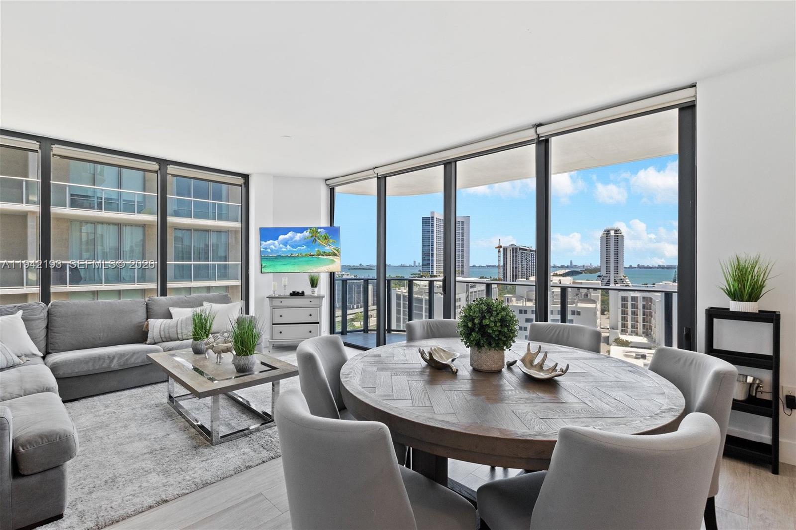 A modern living and dining area features floor-to-ceiling windows with expansive city and water views — 121 NE 34th St # 1008, Miami FL 33137, MIAMI, FL