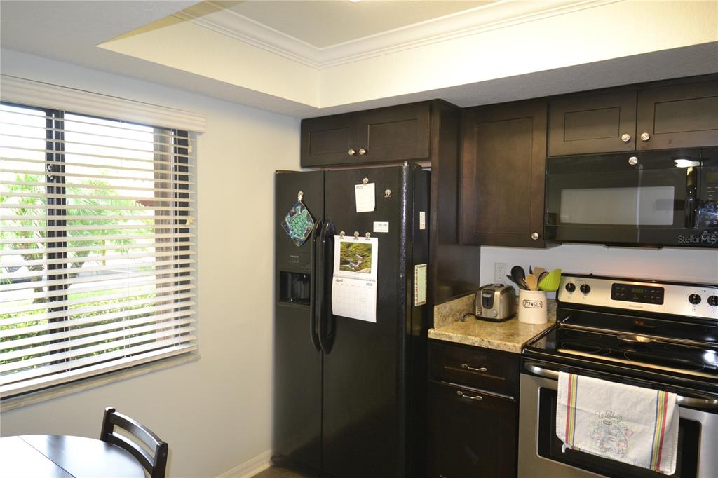 A kitchen features dark wood cabinetry, black appliances, and a window with white blinds — 161 LAKESIDE DRIVE, OLDSMAR, FL