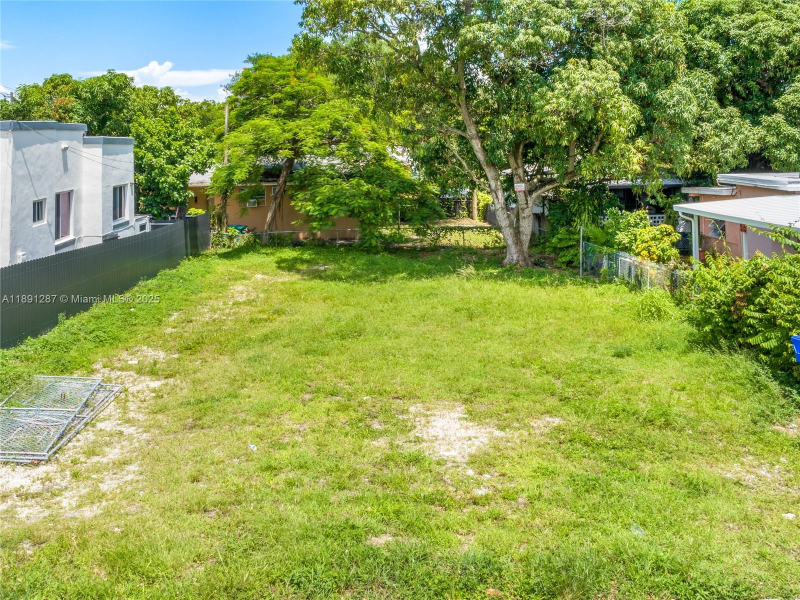 A grassy vacant lot is enclosed by fences and surrounded by trees and neighboring houses — 1881 NW 4th St, Miami FL 33125, MIAMI, FL