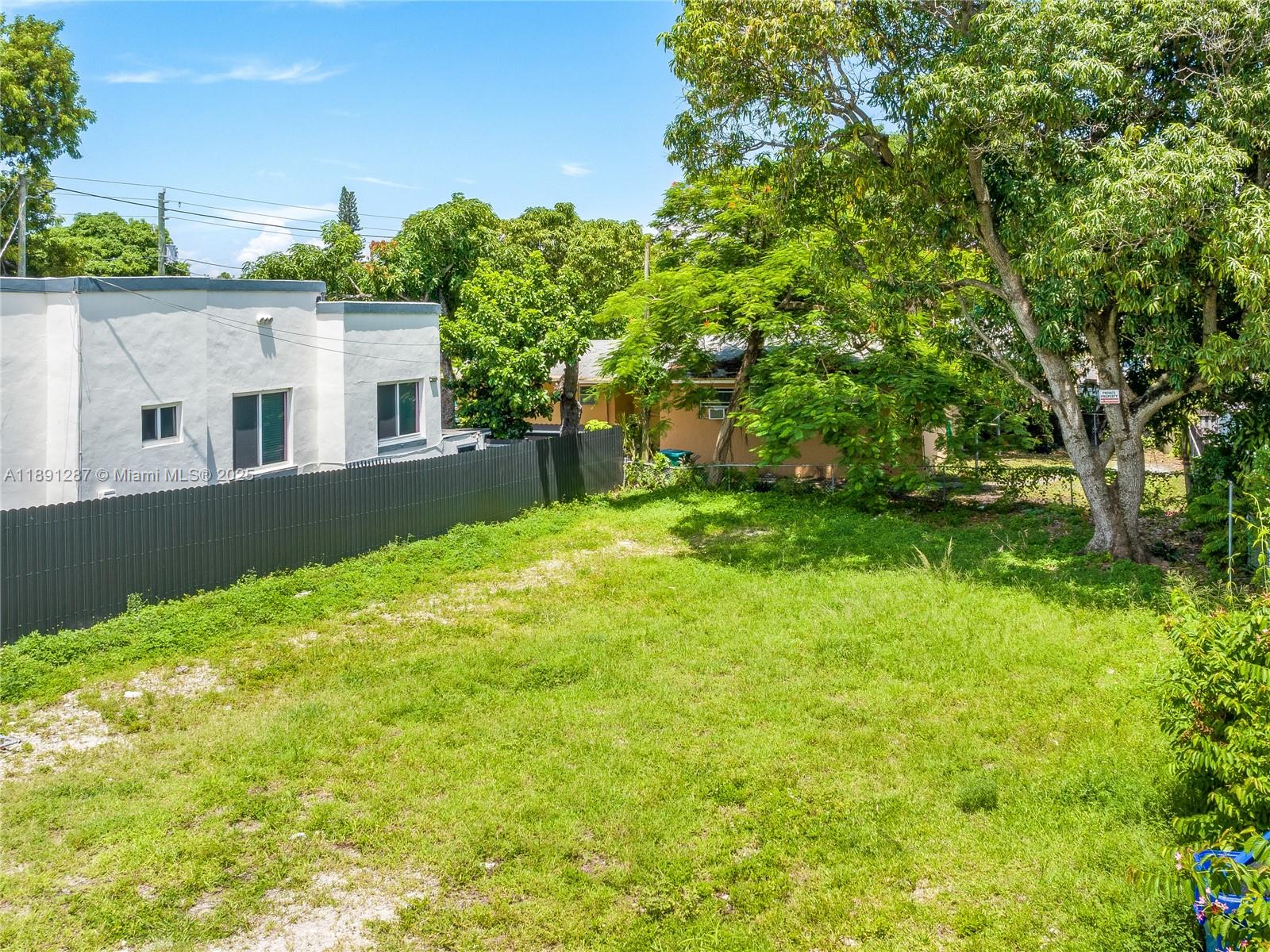An empty, grassy residential lot is enclosed by a gray fence next to a house — 1881 NW 4th St, Miami FL 33125, MIAMI, FL