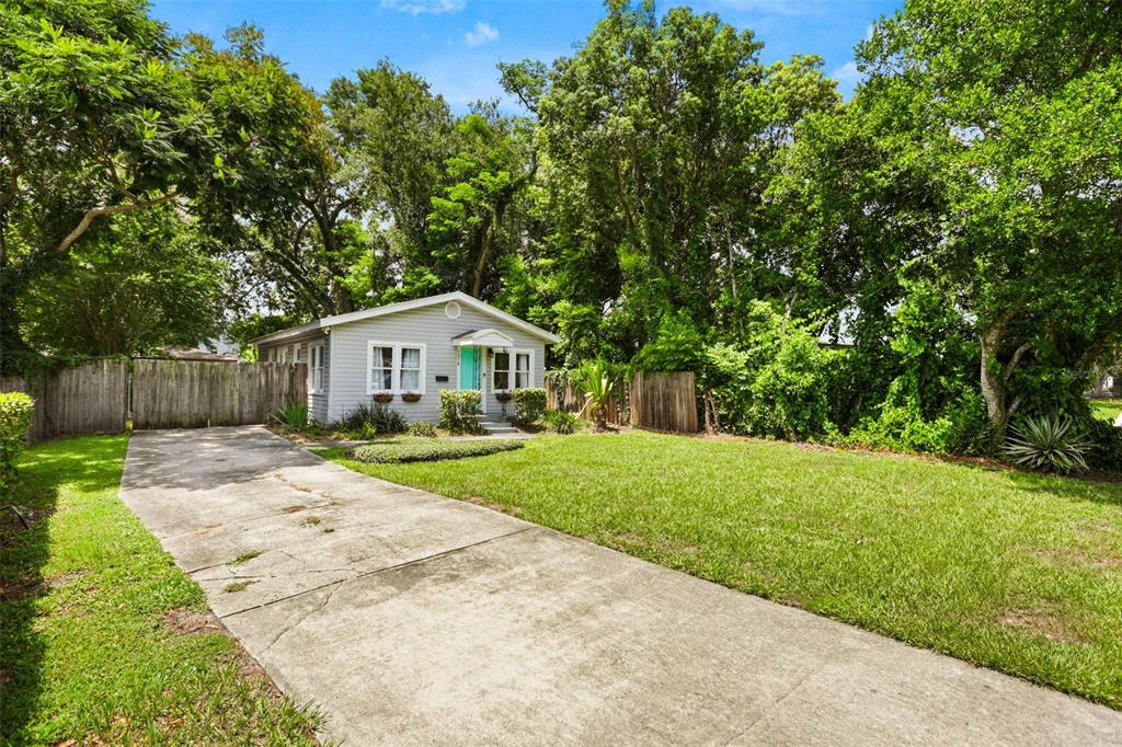 A small, light-gray house with a turquoise front door sits behind a concrete driveway — 1214 E HARDING STREET, ORLANDO, FL