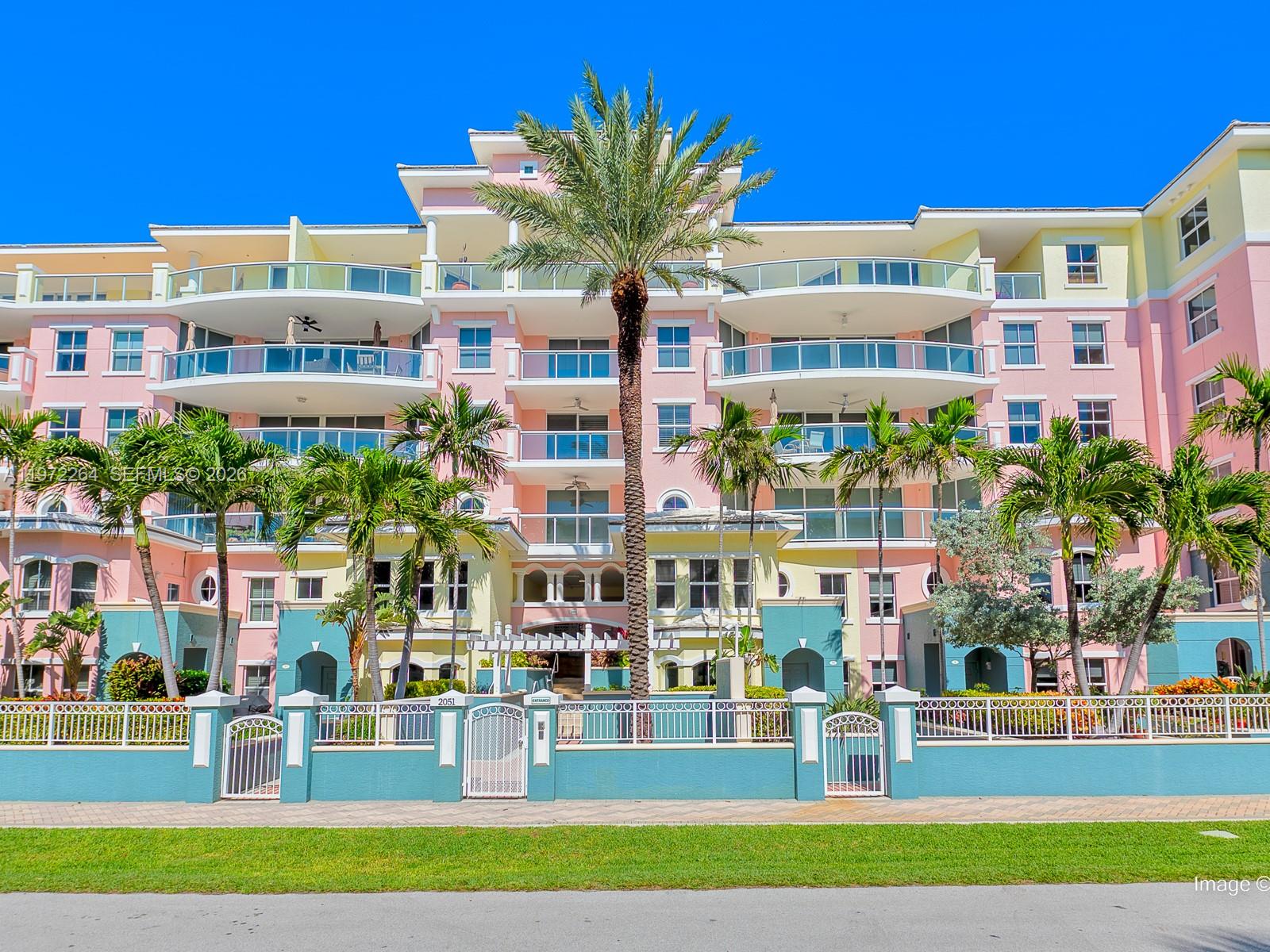 A multi-story pink and yellow apartment building features balconies, palm trees, and a gated entrance — 2051 SE 3rd St, Deerfield Beach FL 33441, DEERFIELD BEACH, FL