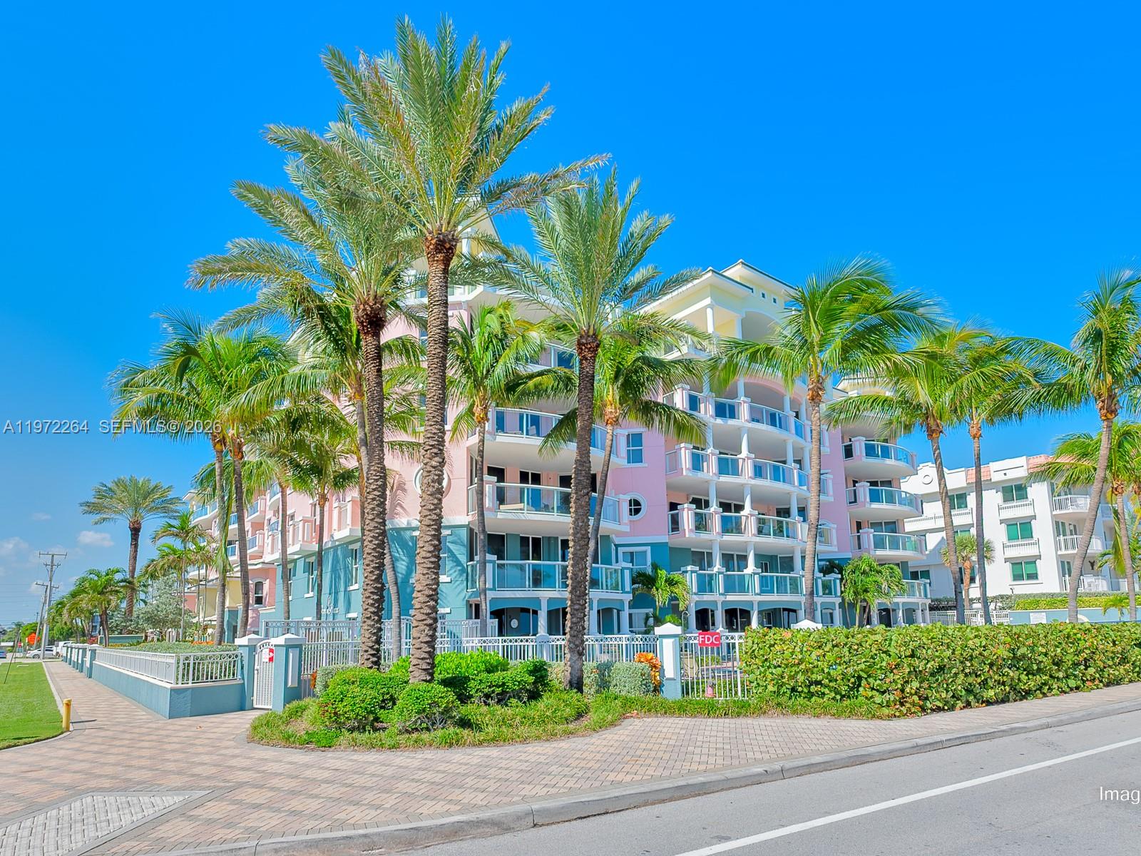 A multi-story pink and teal apartment building is surrounded by palm trees and landscaping — 2051 SE 3rd St, Deerfield Beach FL 33441, DEERFIELD BEACH, FL