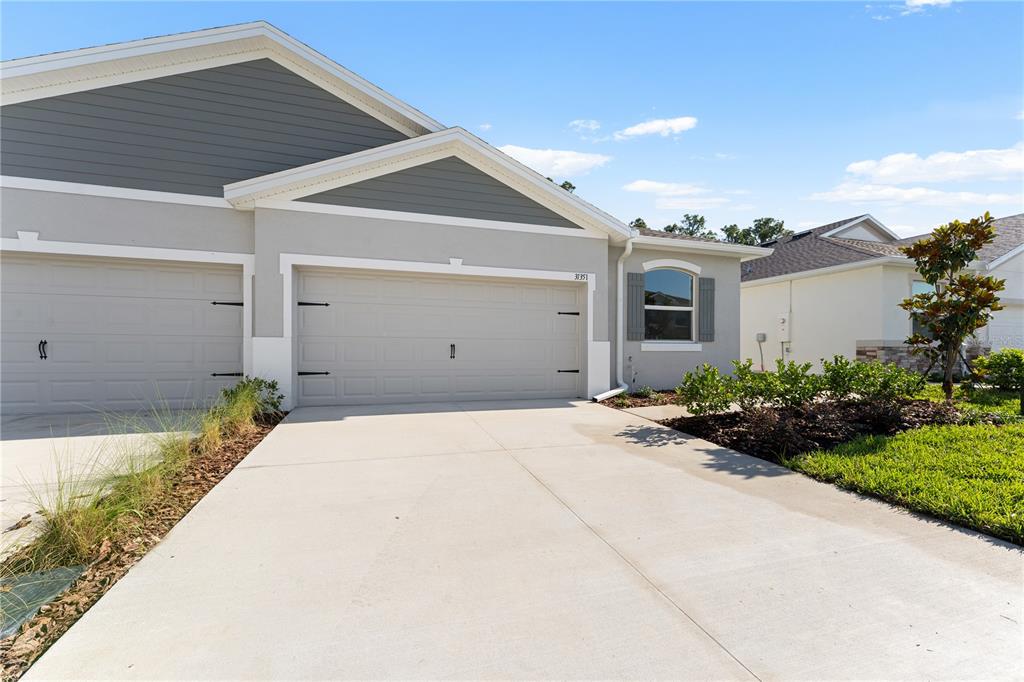 A view of a suburban house exterior featuring a two-car garage and a concrete driveway — 31351 PAPER BIRCH STREET, WESLEY CHAPEL, FL